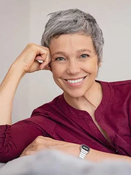 Smiling woman with gray hair wearing burgundy shirt against neutral background, professional headshot.