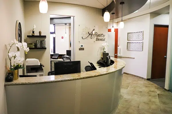 Modern dental office reception area with curved white desk, pendant lighting, and waiting area at Affinity Dental Queen Creek.